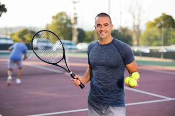 Positive adult sportsman looking at camera while playing tennis at court outdoor