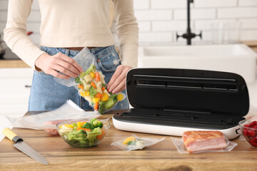 Young woman with vacuum sealer machine for food, meat and vegetables in packs on kitchen table