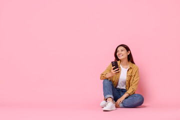 Smiling young woman with smartphone on pink background. Space for text