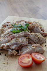 Raw chicken wings with spices, tomatoes and cilantro on a wooden cutting board. Vertical format.