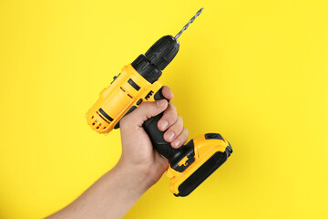 Man with cordless electric drill on yellow background, closeup