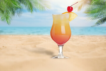 Summer beach with delicious Tequila Sunrise cocktail, palm leaves and golden sand