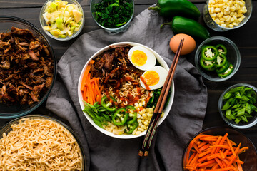 Pork Ramen Topped with Vegetables and a Hard Boiled Egg: Ramen noodles with carrots, scallions, hot peppers, and more served in a bowl with chopsticks