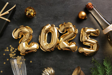 Figure 2025 made of foil balloons with Christmas balls, gift box and bottle of champagne on black background
