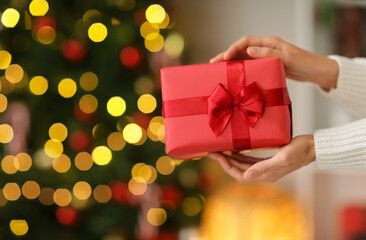 Woman giving gift box near Christmas tree at home, closeup