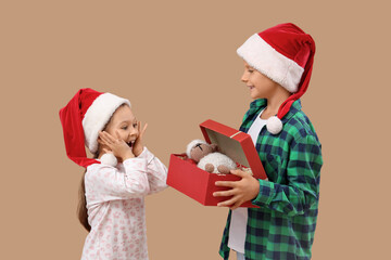 Cute little children in Santa hats opening Christmas gift on beige background
