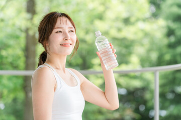 公園・森林の中でミネラルウォーターを飲む若いアジア人女性
