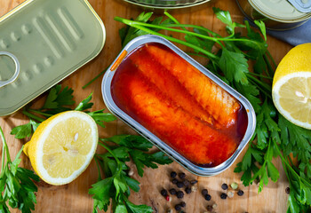 Canned sea fish, mackerel fillets in tomato served with herbs and lemon on wooden table