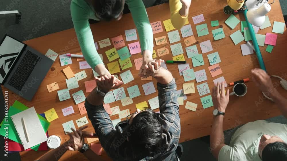 Poster top view of business team giving high five to celebrate project while standing at table with sticky 