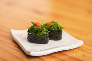 Two pieces of seaweed salad sushi, topped with orange roe, served on a ceramic plate.