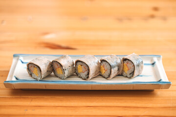 Five sushi rolls with fish, egg, and rice served on a ceramic tray.