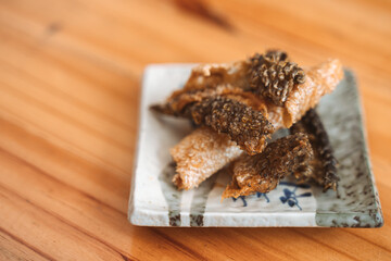 Crispy fried fish skin served on a decorative ceramic plate as a snack or appetizer.