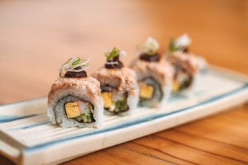 Gourmet sushi rolls topped with sauce and garnished with spring onions on a ceramic tray.