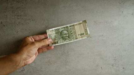 Man holding a 500 rupee indian banknote against a concrete background with a focus on the hand and the bill.