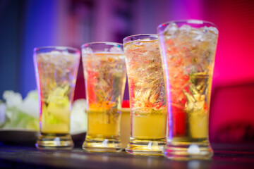 A cold beer glass sits on a cluttered desk during a late-night party, its golden hue reflecting the...