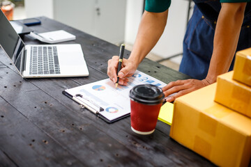 close-up of a man's hands working meticulously with a cardboard box on wooden desk, representing an online seller effort to pack products, successful business operations and customer satisfaction.