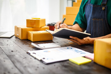 close-up of a man's hands working meticulously with a cardboard box on wooden desk, representing an...