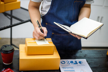 close-up of a man's hands working meticulously with a cardboard box on wooden desk, representing an...