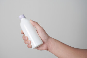 Male person hand holding white bottle, over grey