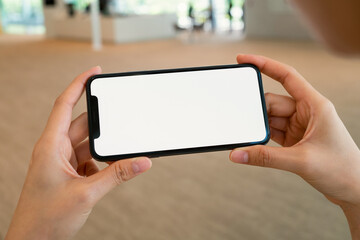 Hand holding black smartphone with blank screen for graphic display montage at shopping mall background.