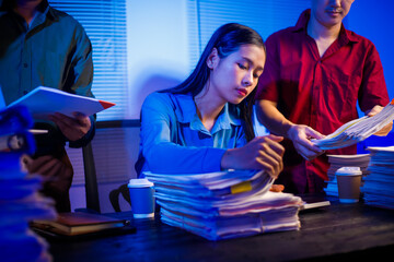 businessman and an Asian businesswoman work late into the night at the office, stressed and busy,...