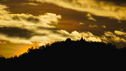 Beautiful sunset landscape over dramatic mountain silhouettes with golden sky and clouds in the background.
