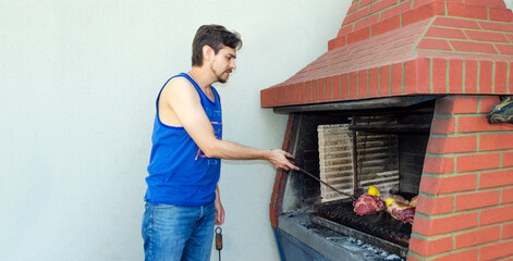 Hombre asando carne a la parrilla, usando un trinche o tenedor, en Buenos Aires, Argentina.