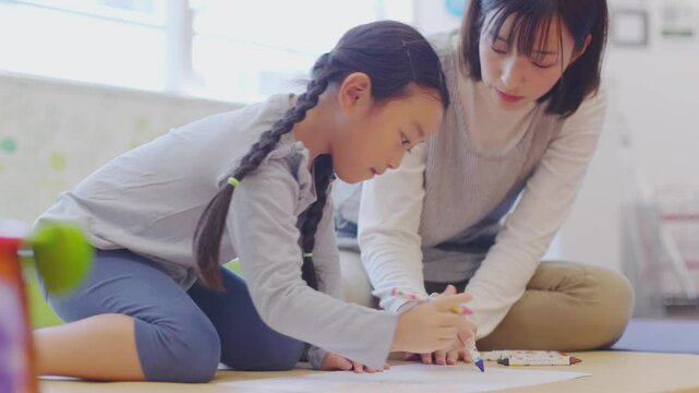 保育園で園児と一緒にお絵描きをする女性保育士	
