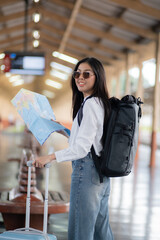 Young woman female smiling traveler with back pack looking to map while waiting for the train at train station, A woman is standing at a train station with a map in her hand