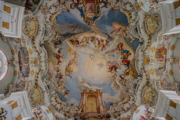 Ornate baroque ceiling fresco depicting a vibrant religious scene with angels and saints in a detailed, golden-framed church interior..
