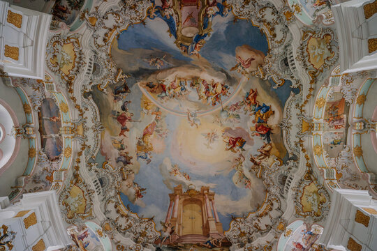 Ornate baroque ceiling fresco depicting a vibrant religious scene with angels and saints in a detailed, golden-framed church interior..