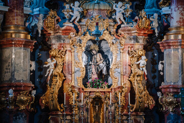 An ornate baroque altar with intricate gold detailing, religious statues, and a central depiction of Jesus, set in a richly decorated church interior..