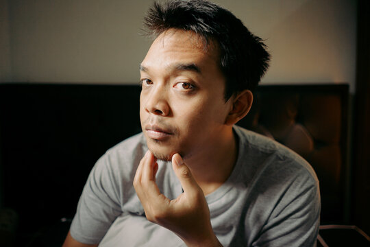 A man examining his facial hair while touching his chin, appearing thoughtful and focused