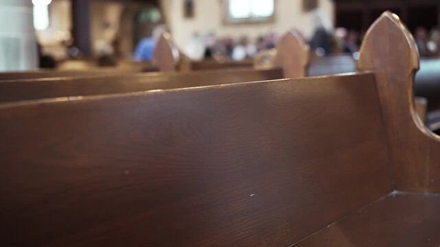 Slow-motion dramatic shot of empty wooden church pews with people in the background ready for mass to start.