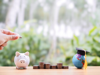 Hand putting coin into piggy bank, Earth globe with graduation hat and stack of coins. The concept of saving money for education, student loan, scholarship, tuition fees in the future