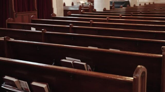 Slow-motion dramatic shot of empty wooden church pews with columns in the background.