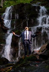 Successful electronic waterproof. Business man in suit with laptop at waterfall background. Telework stressful work concept.