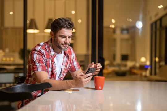 Man relaxing sitting on couch while looking at mobile phone. Mature man using smartphone to checking email at home. Handsome young man using his smart phone while sitting on the couch at home.