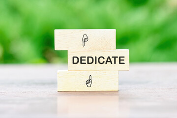 DEDICATE word written on wooden bars on a green background of plants out of focus