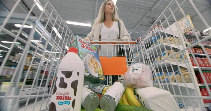 Caucasian Woman Placing Groceries Into Her Trolley in a Supermarket Aisle, Ensuring a Balanced Selection of Fresh Produce, Dairy, and Packaged Goods. Timelapse Footage From Inside the Shopping Cart