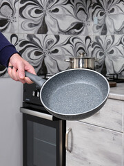 Man holding empty non-stick frying pan in hand against home kitchen background. Modern cookware for cooking at home.