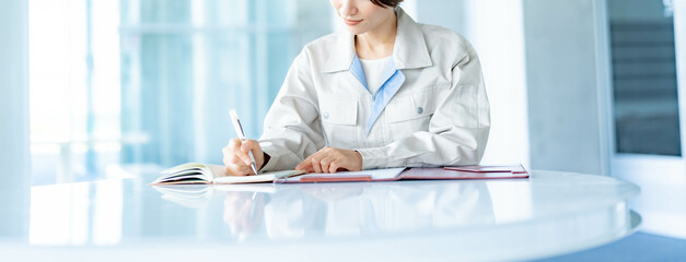 資料にペンで書く作業着を着た女性