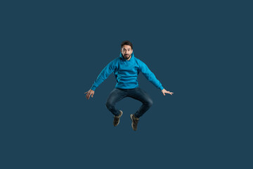 Obraz premium A man in a blue hoodie is mid-air, leaping with joy. The dark background emphasizes his vibrant outfit and energetic pose, showcasing an expression of excitement and freedom.