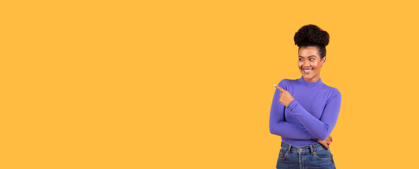 A woman in a purple sweater stands confidently with her arms crossed, pointing to copy space with a smile. The bright yellow backdrop adds a cheerful atmosphere to the moment.