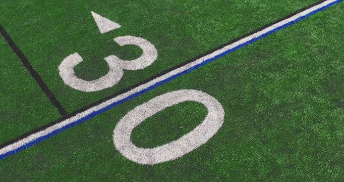 Aerial video of a typical synthetic turf football field 30 yard line in white.	