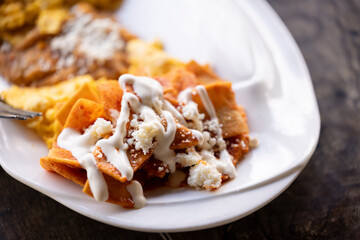 Morning sun shines on a plate of Chilaquiles Rojos, eggs, and beans on a table.