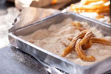 Freshly fried churros rest in a pan of cinnamon and sugar.