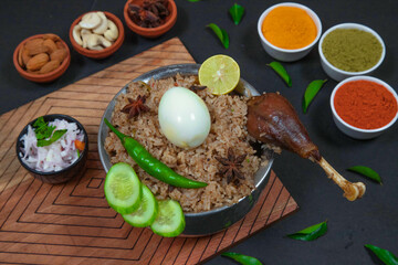 mutton biryani, leg piece biryani, chicken biryani along with cucumber slice, onion, onion raita, capsicum, cashews, almond, green peas, egg, chili powder, coriander powder and spices on silver bowl