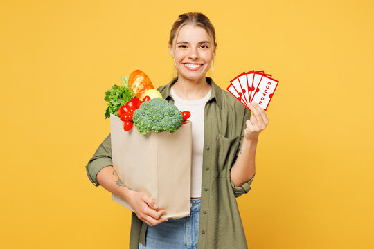 Young happy fun woman wear casual clothes hold bag for takeaway mock up with food products, store gift certificate coupon voucher card isolated on plain yellow background. Delivery service from shop.