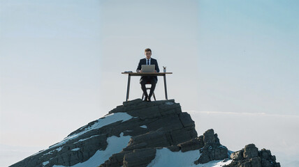 Businessman working remote work on a laptop at a desk on a mountain peak under clear sky.